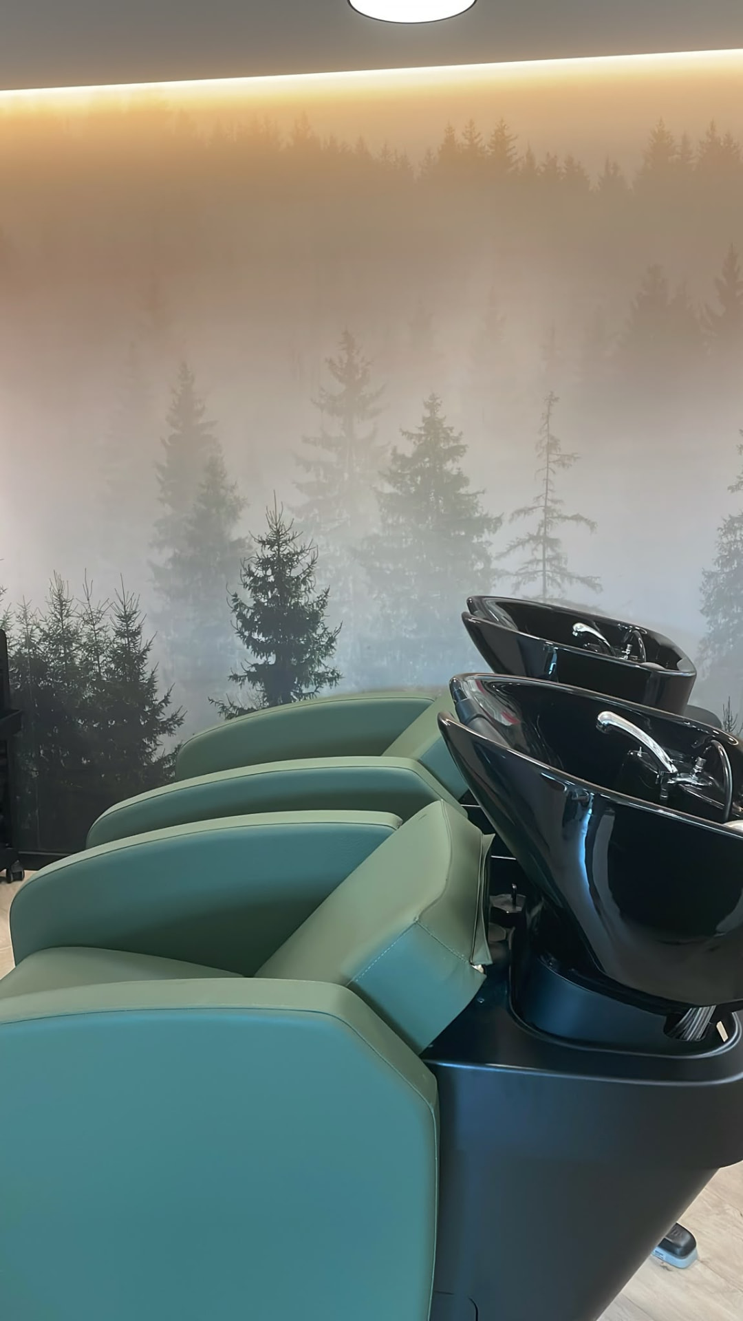 Waschbereich im Salon Melanie B mit grünen Waschsesseln und Waldmotiv